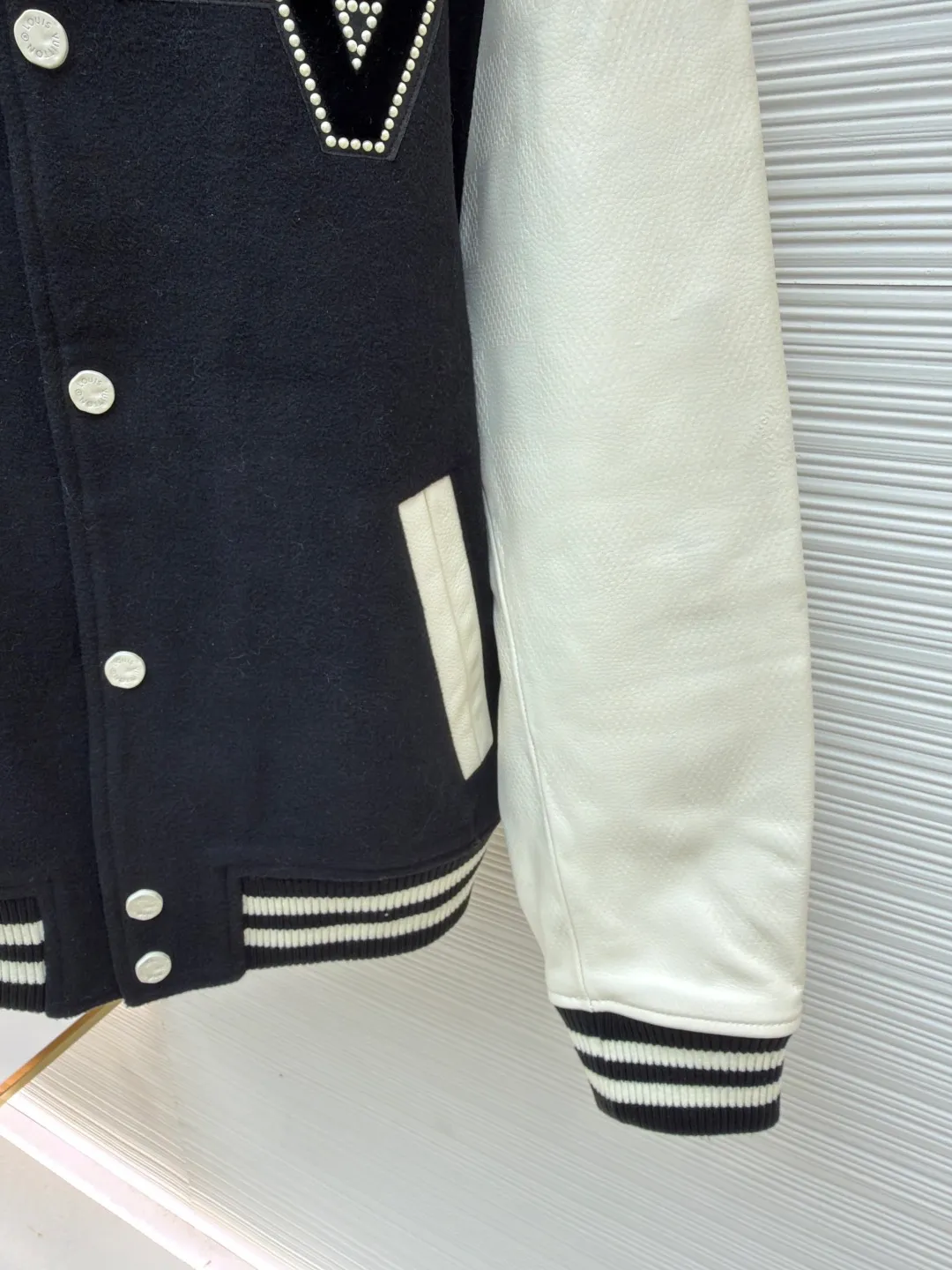 LOUIS VUITTON checkerboard embossed genuine leather and wool baseball jersey ●Original version: 51000 purchased and developed ●Item number: 1680926-i15 ●Fabric: genuine leather wool fabric ●Technology: embroidery ●Version: fitted version ●Weight: about 1770 grams ●Size: 44-46-48-50 ●Description: The fabric is made of 80% wool, with a weight of 750g. It is made of newly sheared wool and is dyed in reactive black in the vat. The colored cloth is bristle process. After brushing 5 times and washing 6 times, the fluffy surface fluff is trimmed flat, and the surface of the fabric appears fluffy. It has a hollow three-dimensional fluffy effect. You can feel the elasticity of the fabric when you touch and press it with your hands. The newly sheared wool yarn is long-fiber and is not easy to pill after shearing. The front and back panels are embroidered with Tajima embroidery machines imported from Japan. The nylon material is super matte and the tatami stitch method is multi-layered. Overlapping thread embroidery, the front chapter is made of viscose yarn, three-dimensional toothbrush embroidery, the mold is opened to determine the pile height and the suede is smoothed by hand, using acrylic round bubble beads, the surface of the bubble beads is sprayed three times, the base paint is latex paint, and the middle layer is sprayed with pearls Pearl white paint, the outer layer is sprayed with translucent glossy paint, the translucent bright white effect is completely comparable to that of mother-of-pearl. There are a total of 154 beads in the chapter. Each bead is dusted and positioned to ensure that it is flush with the edge of the chapter. The visual effect is not obtrusive. The two sleeves are made of water Made of dyed cowhide. Compared with spray-painted cowhide, there is nothing attached to the surface of water-dyed cowhide. Pure water-based dyes are continuously stirred in the tank to naturally color. During the period, samples are taken to compare the color of the Y-version sleeves according to the degree of coloring. When the colors are basically the same, they can be washed and dried naturally to produce the finished product. The thickness of the finished leather is 12mm. The embossing is made of a large-size aviation aluminum plate material mold. All the flowers are pressed according to the code positioning. An electric hydraulic control system is used, and the constant temperature and timing are automatically operated. The small sleeve logo is embossed separately from the small mold. It is pressed by electromagnetic pulse pressure and heating. After the sleeves are cut and embossed, the leather base is all shoveled to a thickness of 8mm. The leather thickness is reduced and the hand feels softer and closer to the body. The diamond-shaped plaid embossing on the surface causes an anti-skin phenomenon due to the thinning of the leather base. The pattern will naturally increase from the deep base state. Lightened, the diamond check pattern and the leather pebbles form a visually invisible effect. It is matched with cupro + cotton blended lining, the ribs are made of combed cotton yarn, and the horizontal loom imported from Taiwan has inter-color jacquard. It is matched with a custom-made molded aluminum alloy material with a logo spray-painted four-button buckle.